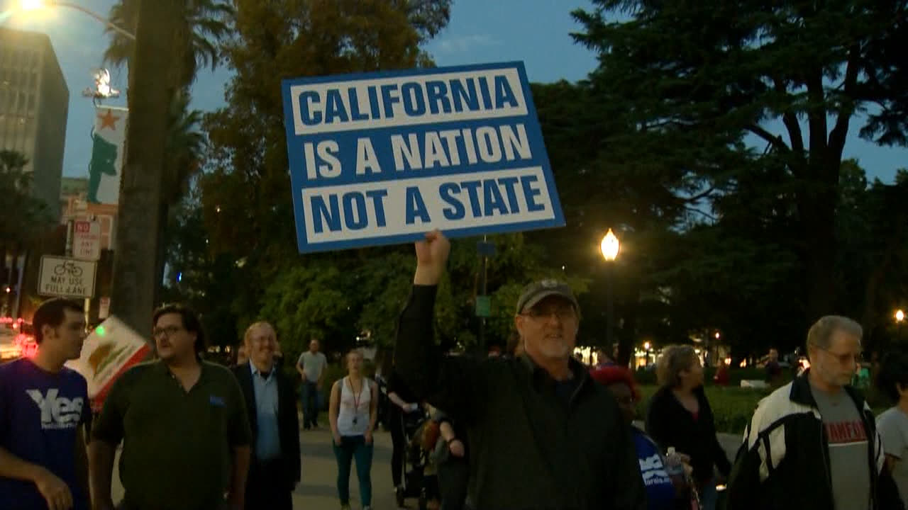 Supporters marching at dusk, one holding a sign reading "California is a nation not a state", with California state flags among the crowd